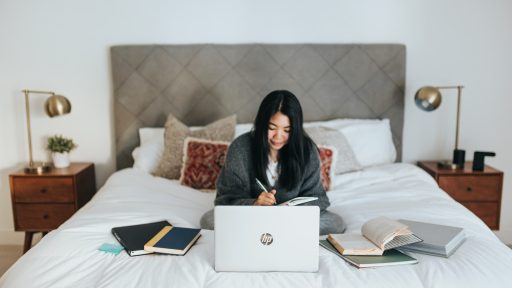 woman in black hijab sitting on bed using laptop